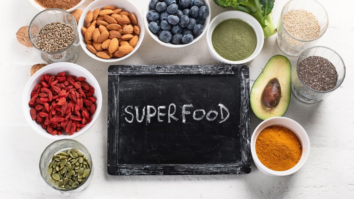Assorted superfoods including berries, seeds, avocado, nuts, and green powders arranged around a chalkboard labeled “superfood”