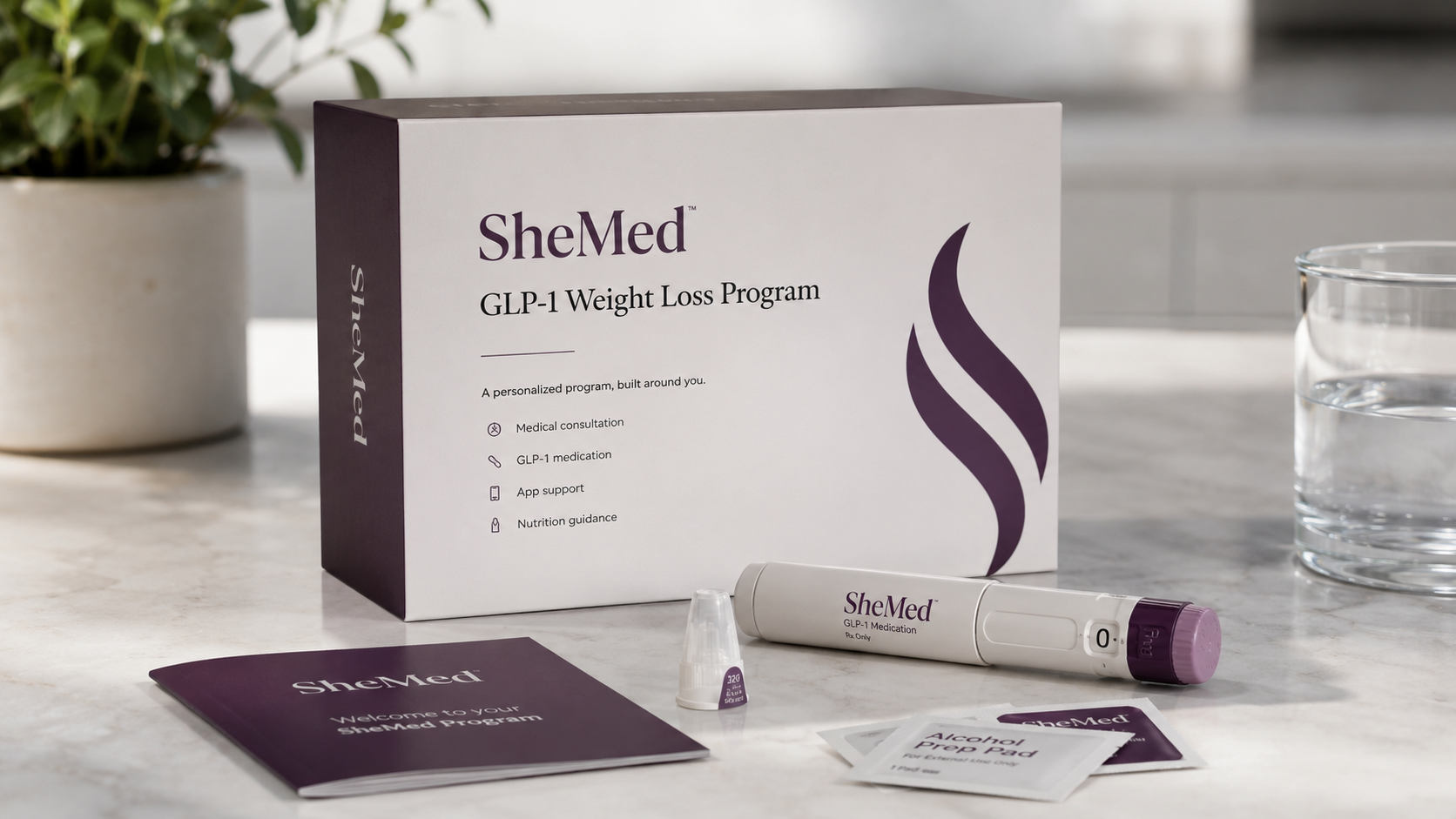 SheMed GLP-1 Weight Loss Program kit displayed on a marble countertop with branded packaging, a GLP-1 injection pen, alcohol prep pads, and a welcome booklet in a softly lit modern kitchen setting.