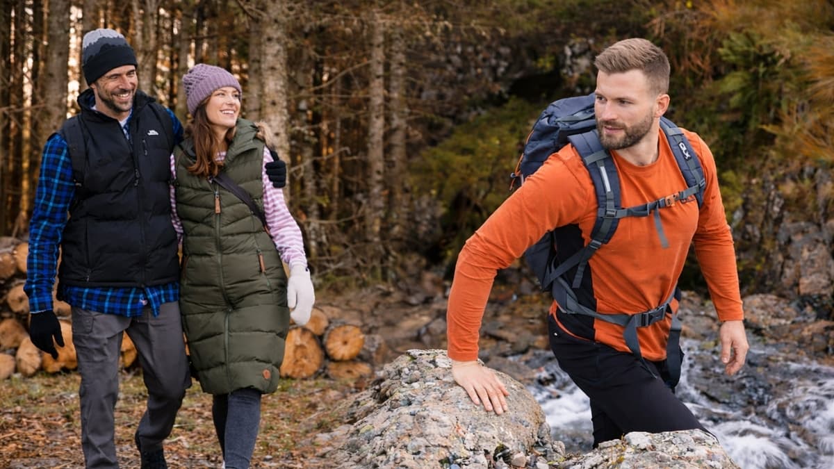 Hikers wearing Trespass outdoor jackets and backpacks crossing a forest stream trail