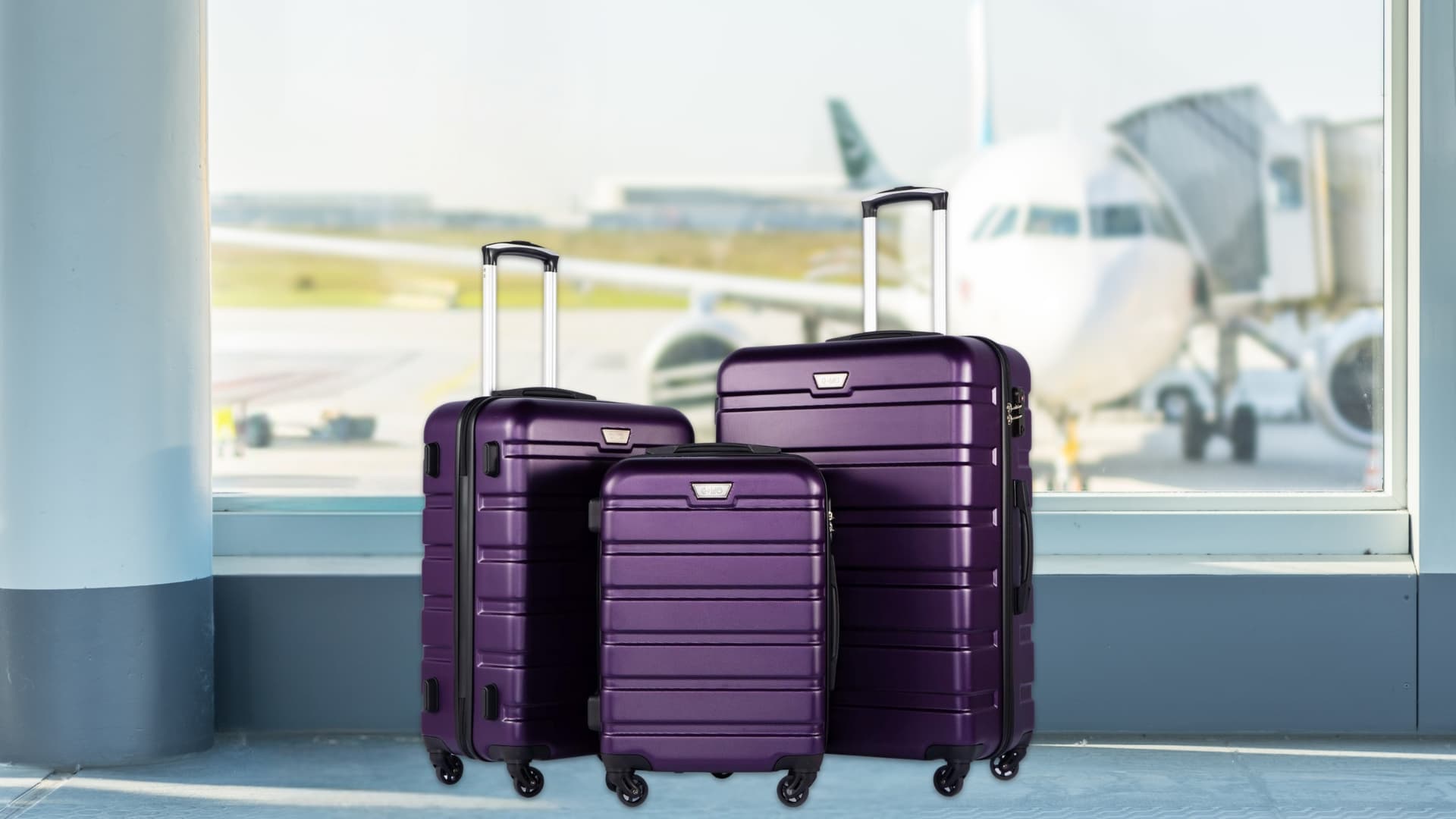 A purple 3-piece hardshell luggage set with spinner wheels stands in an airport terminal near a window, with a plane visible in the background.