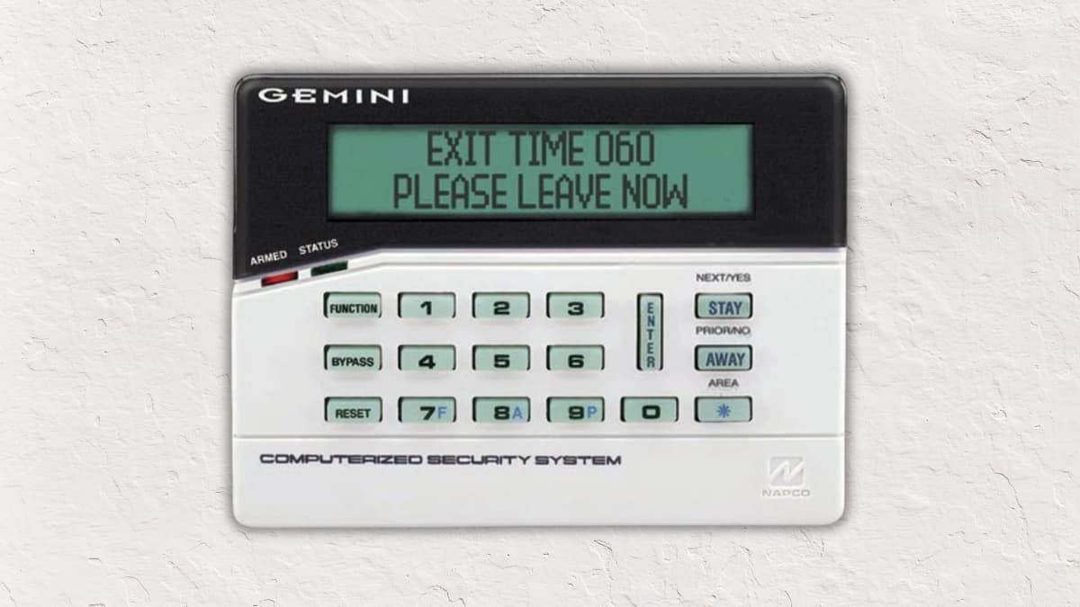 Alphanumeric Napco alarm keypad showing exit countdown and leave message on backlit screen.
