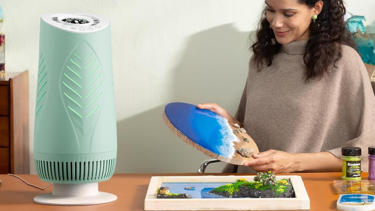 Woman working on resin art next to a Resiners Purair air purifier on a craft table.