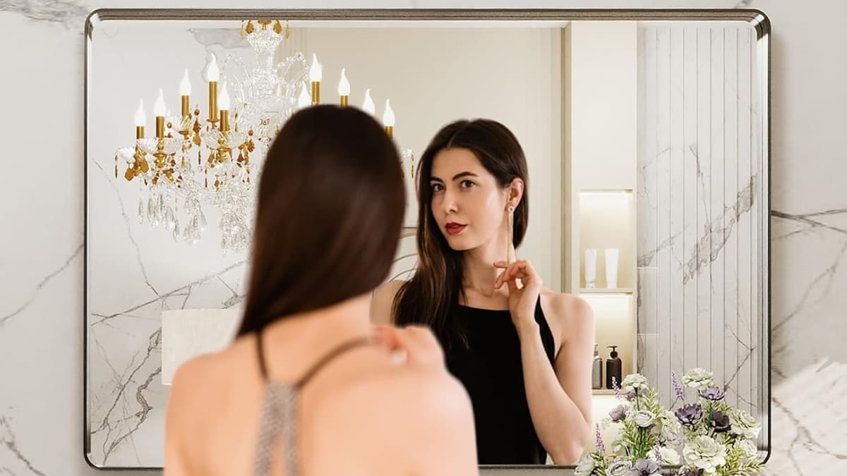 Woman looking into a LOAAO brushed nickel bathroom mirror with marble walls and a chandelier
