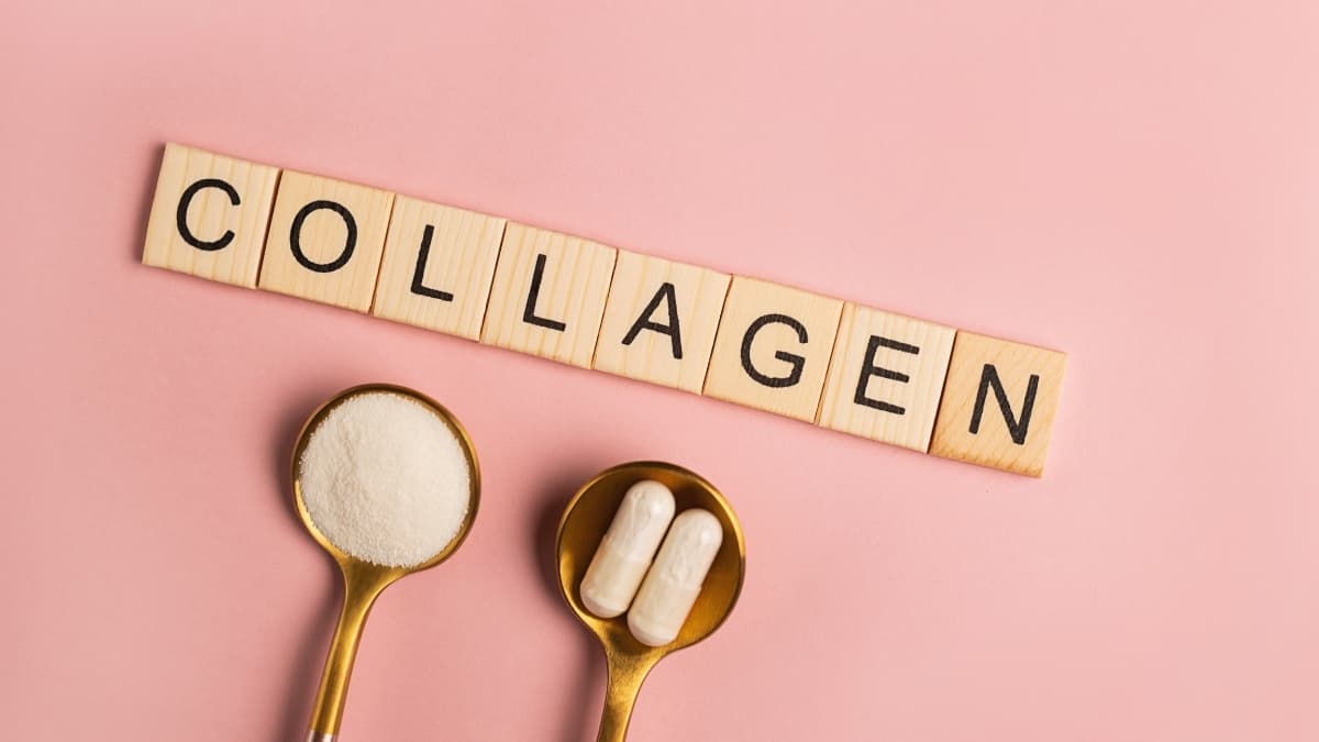 Collagen powder and capsules displayed on gold spoons with wooden blocks spelling “collagen” on a soft pink background