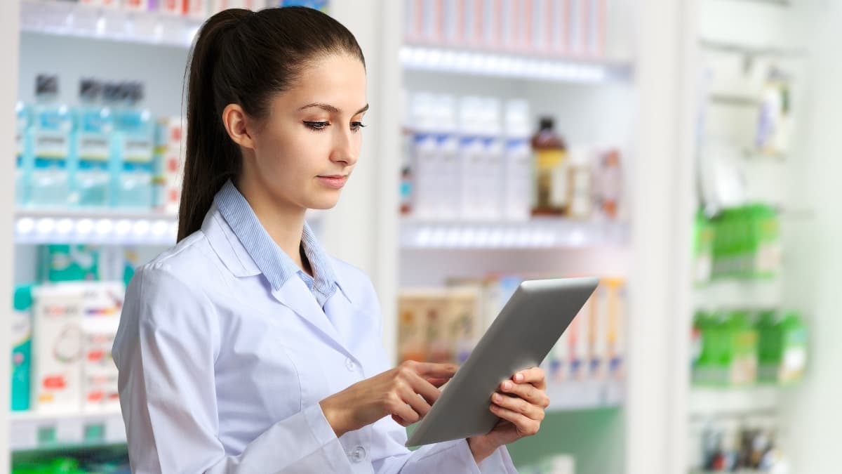 Pharmacist using tablet in modern pharmacy checking online prescription order shelves in background