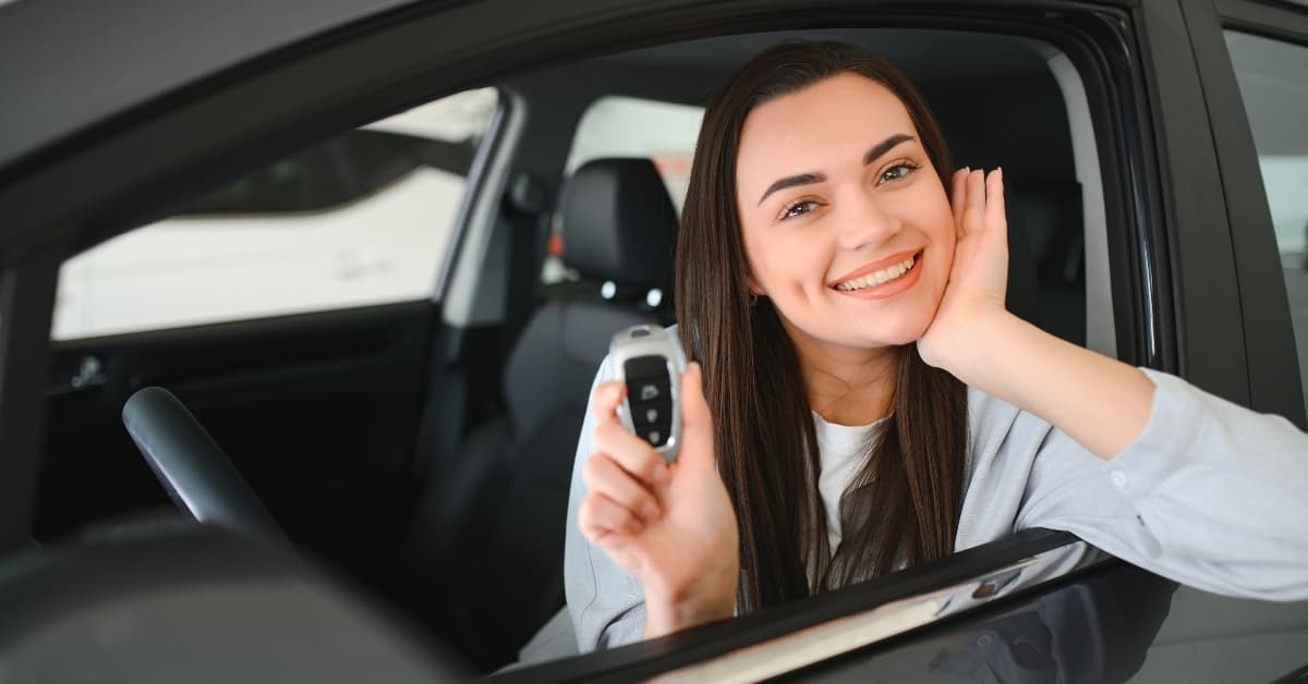 Smiling woman sitting in a rental car holding car keys, representing easy and reliable car rental service.