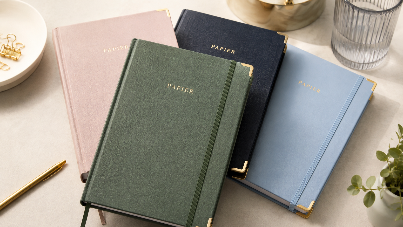 Papier personalized planners in green, pink, navy and blue with gold detailing, styled on a minimalist desk.